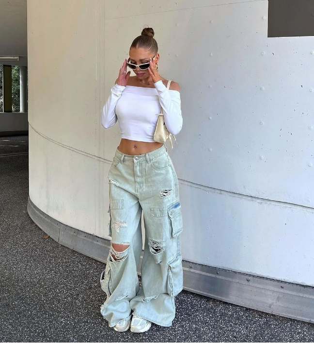 Girl wearing a off-the-shoulder white crop top with light blue distressed ripped cargo jeans