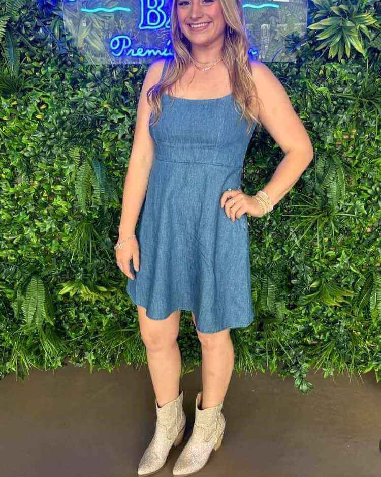 Hanna wearing a sleeveless blue denim dress with metallic cowboy boots