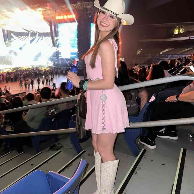 Girl wearing a charming pale pink sleeveless dress with a flared skirt and white hat with white cowboy boots