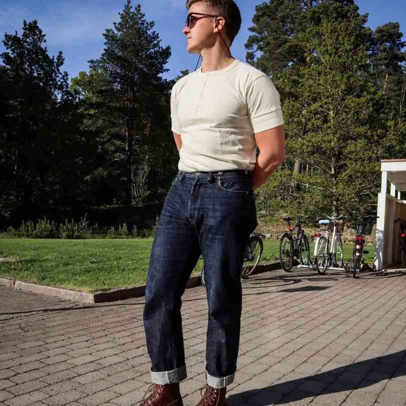 Guy wearing a cream-colored Henley shirt with dark blue denim jeans and lace up leather boots