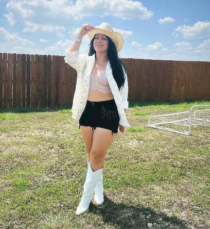 Laura wearing a soft pastel color lace bralette underneath a white button up shirt with black shorts