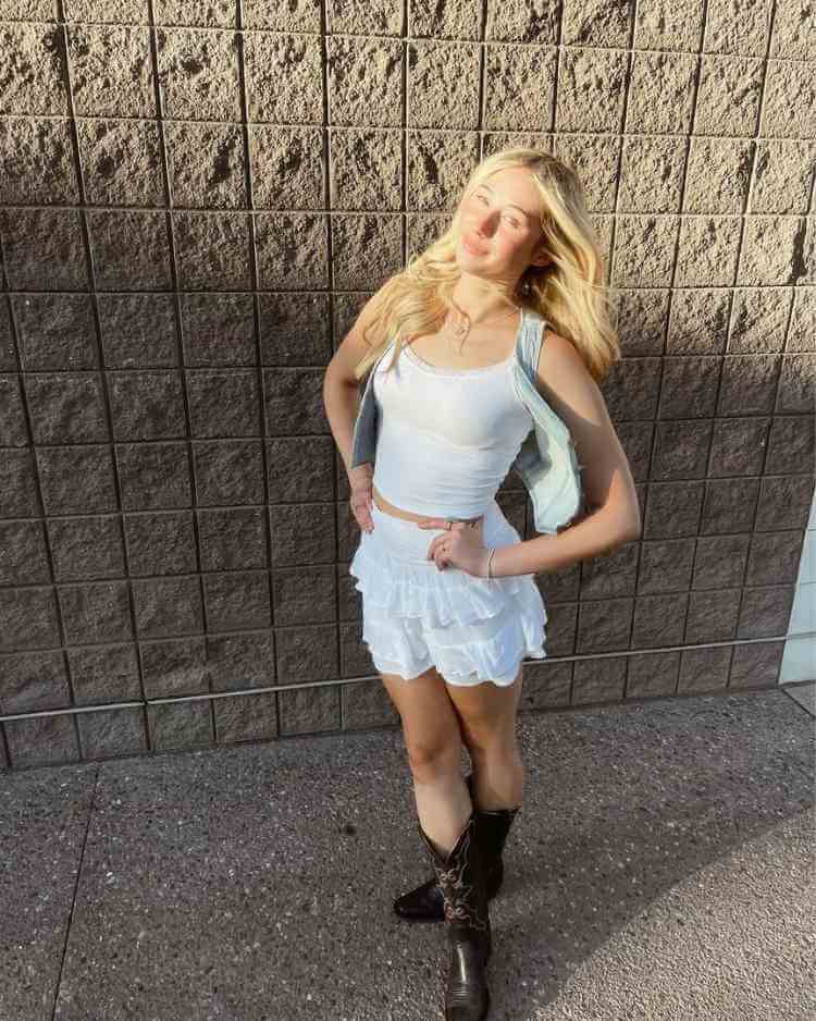 Missy wearing a pale blue vest over a white tank top with teired mini skirt and dark brown cowboy boots