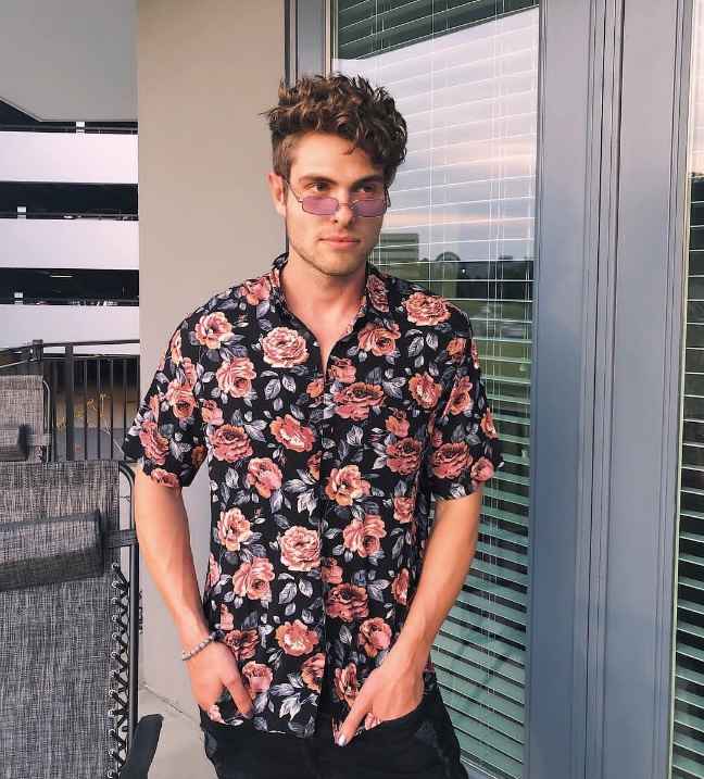 Brandon wearing A black short-sleeved button-up shirt with a vibrant pink floral pattern with black pants