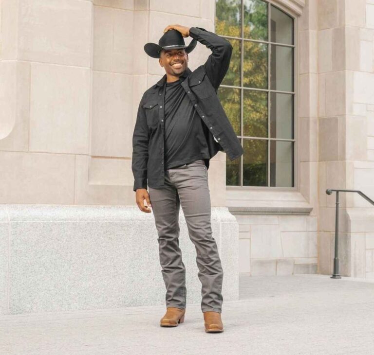 Dan wearing a sleek black button-up shirt layered under a black denim jacket, paired with some slim-fit grey jeans