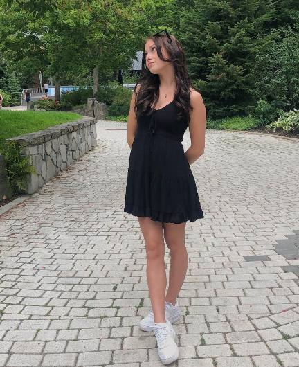 Harlee wearing a black sleeveless mini dress with white sneakers