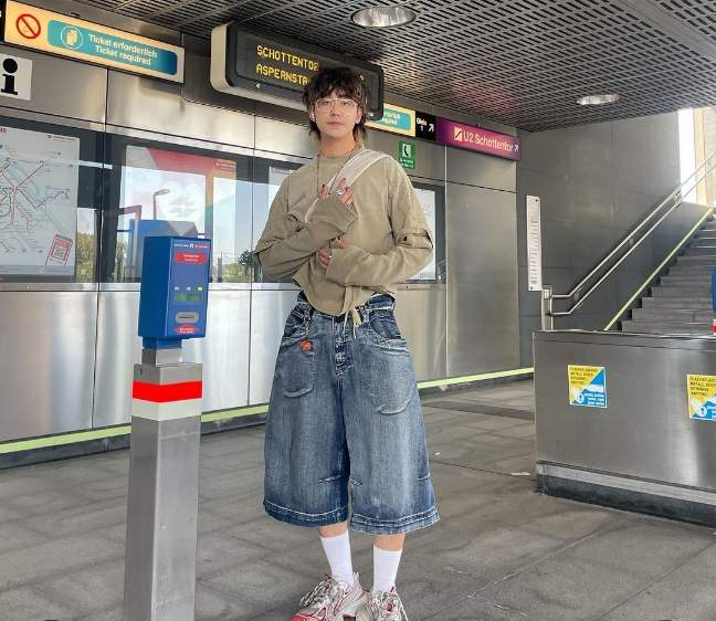 Jojo wearing a loose, beige, long-sleeve shirt with denim culotte shorts