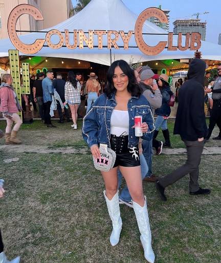 Marissa wearing a blue denim jacket over a white tank top with black high-waisted leather shorts with lace-up detail