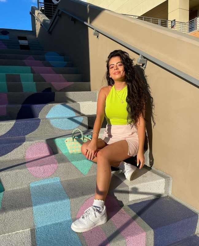 Stephanie wearing a bright yellow sleeveless crop top with a pink mini silk skirt