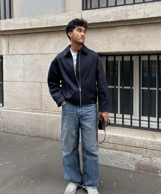 Guy wearing a dark navy blue zip-up jacket over a white tee and loose fitting jeans