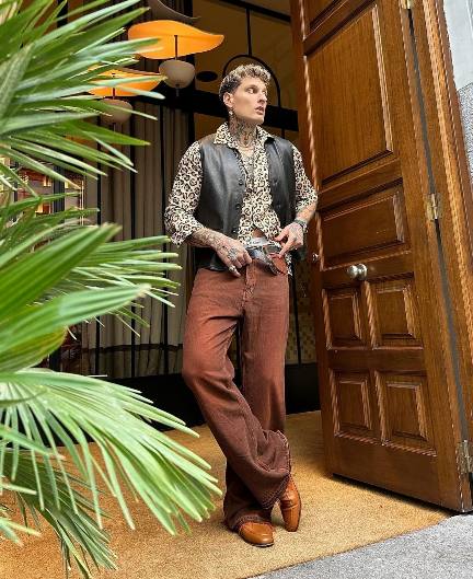 Mihail wearing a leather vest over a leopard print shirt with rust colored pants