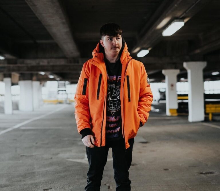 aaran wearing an electric orange jacket over a graphic hoodie wih black booms