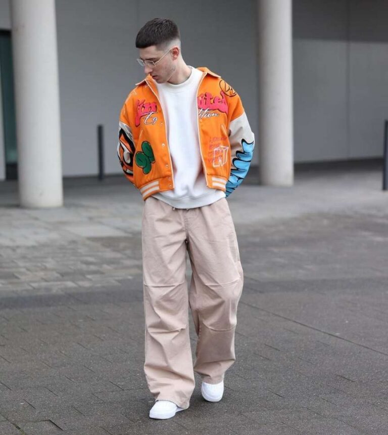 alex wearing a varsity jacket with eye-catching color over a white tee with beige wide-leg pants