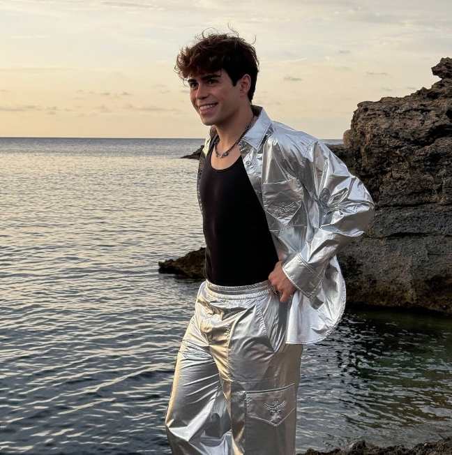 benji wearing a reflective silver jacket over a black tank top with shiny silver pants