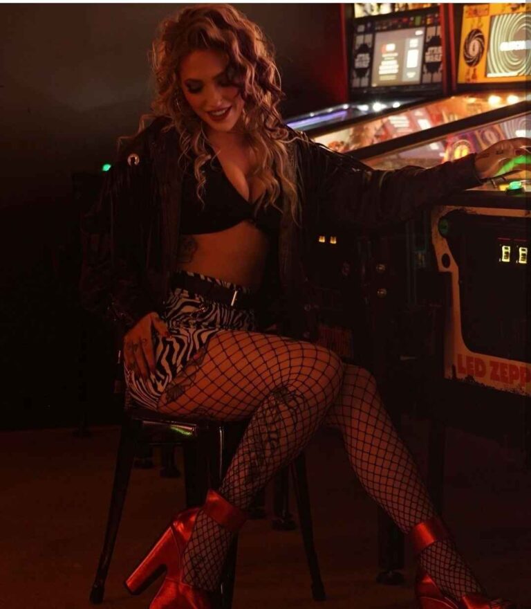 francesca wearing a black leather jacket over a a black bralette, with zebra-print mini skirt, and bold fishnet stockings