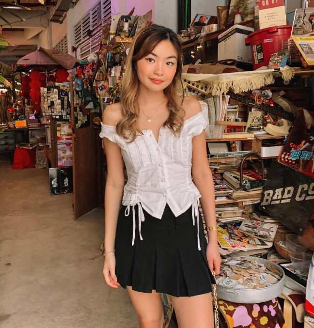 sheryl wearing a white off-shoulder corset top, paired perfectly with a black pleated mini-skirt