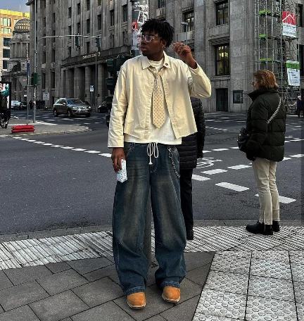 guy wearing a button-down beige shirt over a white tee and blue, dirty-washed baggy jeans