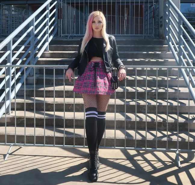 klaudia wearing a black leather jacket over a black crop top with flirty pink plaid skirt