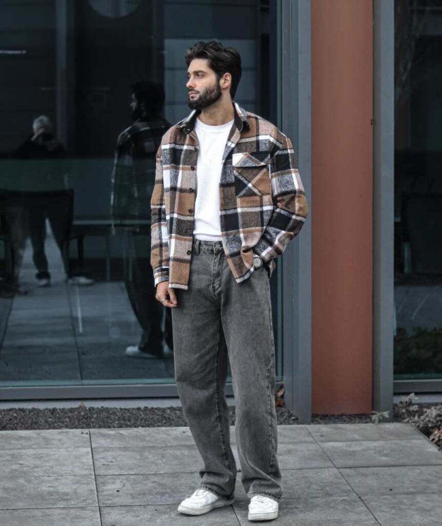 andy wearing A tan, black, and white plaid oversized flannel over A plain white T-shirt with Faded gray straight-leg jeans