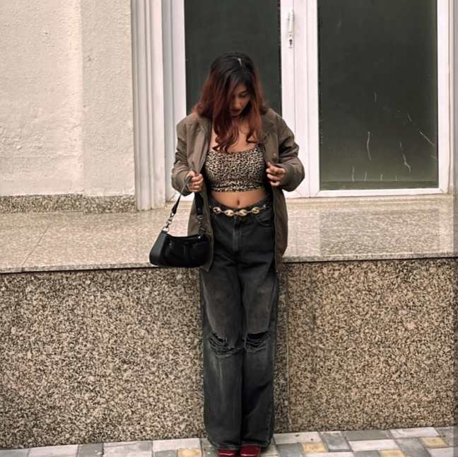 girl wearing a cropped leopard-print top layered under an oversized khaki bomber jacket wide-leg distressed black jeans