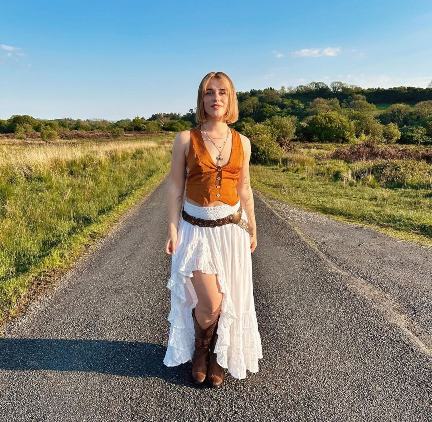 girl wearing a rust-orange sleeveless button-up vest paired with a high-low white maxi skirt