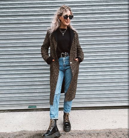 girl wearing a sleek black sweater under a statement leopard-print coat and light-wash jeans with platform Doc Martens