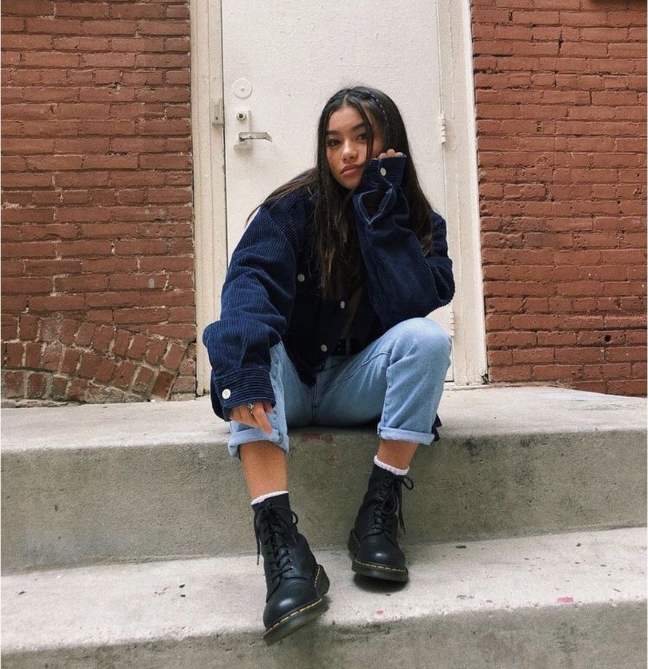 girl wearing simple black top under a navy corduroy jacket with light-wash straight-leg jeans and doc martens