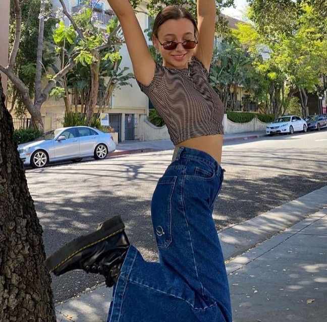 girl wearing wide-leg dark-wash jeans and classic black Doc Martens with a fitted, ruched marble print crop top