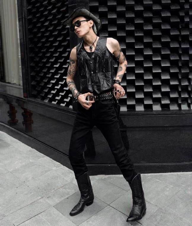 guy wearing A black leather sleeveless vest with fringe detailing layered over a black tank top is paired with slim-fit black pants