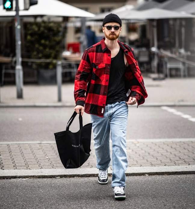 guy wearing A red and black buffalo oversized plaid flannel over a simple black tank top and Light-wash relaxed jeans