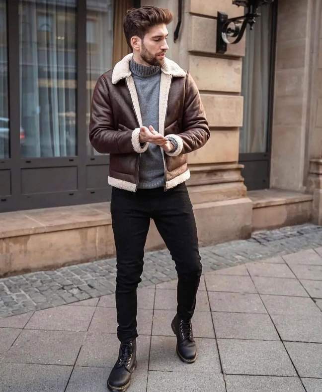 guy wearing a dark brown shearling-lined leather jacket over a gray ribbed knit turtleneck sweater with slim-fit black jeans