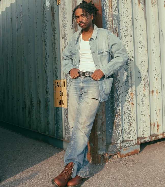 guy wearing alight-wash distressed jeans with a simple white tank top and a relaxed denim jacket and doc martens