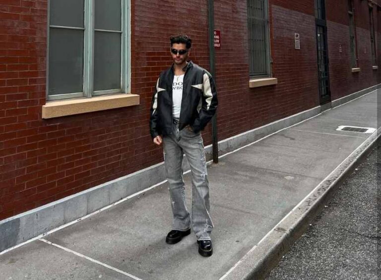 guy wearing black and cream bomber jacket over a vintage-inspired graphic tee with faded grey jeans and doc martens