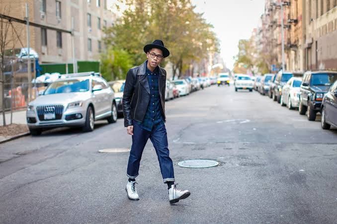 guy wearing navy plaid shirt layered under a black leather jacket with cuffed dark-wash jeans and white doc martens