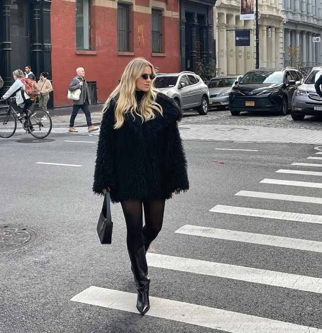 izzy wearing a black shaggy faux-fur coat over a fitted black turtleneck with sheer black tights