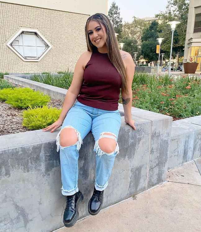 monica wearing A burgundy sleeveless top with light-wash ripped jeans and doc martens