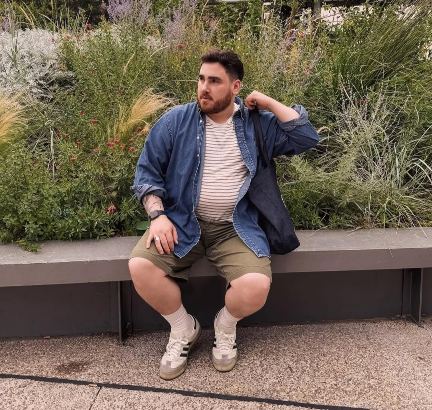 plus size man wearing A striped white and beige T-shirt layered with an unbuttoned medium-wash denim shirt and Olive-green shorts