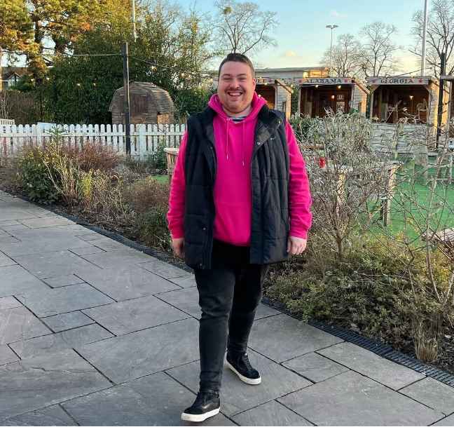 plus size man wearing a black quilted sleeveless vest over a pink hoodie with black slim-fit pants