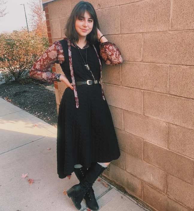 woman wearing A black sleeveless midi dress with a subtle textured design layered over a long-sleeved sheer blouse