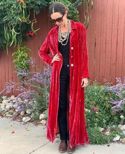 woman wearing A dramatic and luxurious red velvet duster coat worn over a simple black top and high-waisted black jeans