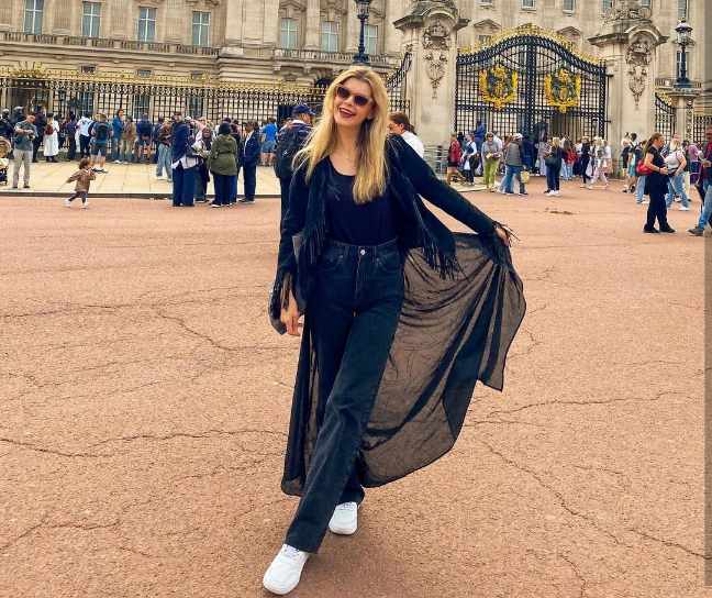 woman wearing a long black sheer duster with fringe details layered over a black top and high-waisted black jeans